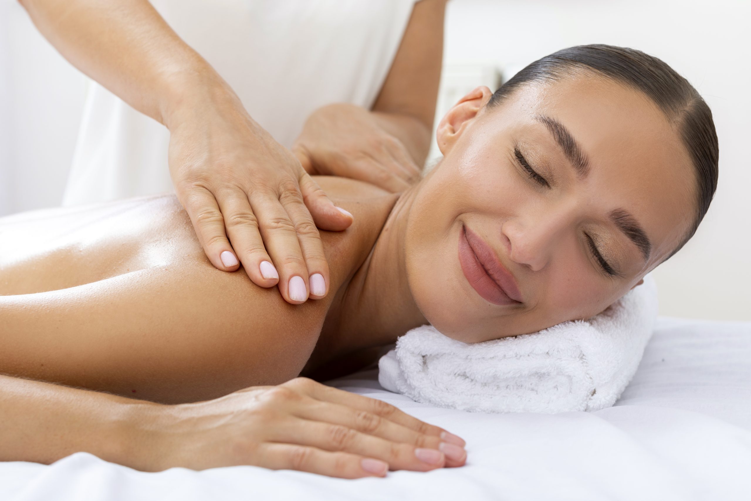 smiling lady getting shoulders massage by professional masseur, lying with closed eyes in luxury beauty salon