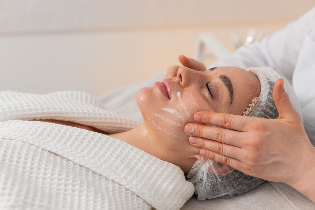 cosmetologist cleanses young woman face with foam cleanser before facial therapy in beauty clinic